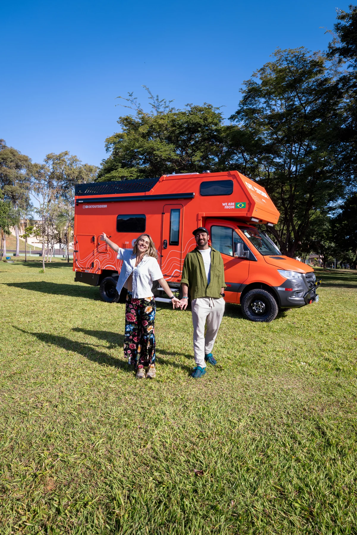 Ale e Duda de mãos dadas em frente ao motorhome laranja GetOutside